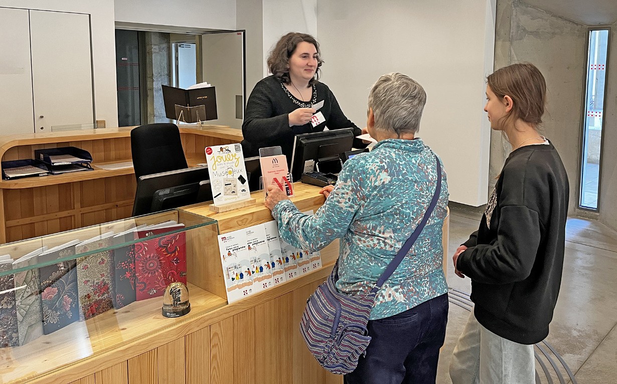 Photo d'une agent d'accueil en train de donner des billets d'entrée à deux visiteuses du Musée Savoisien à Chambéry (une grand-mère et sa petite-fille adolescente)