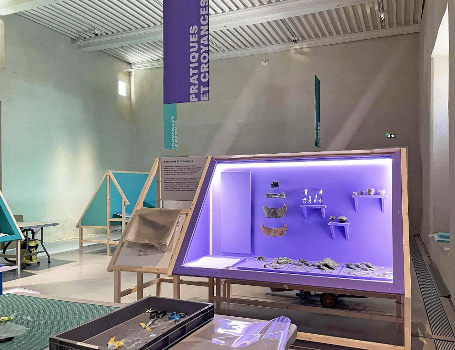 Photo du montage de l'exposition temporaire Bronze, l'âge retrouvé au Musée Savoisien à Chambéry : vue de la dernière salle d'exposition avec une vitrine éclairée et remplie d'objets