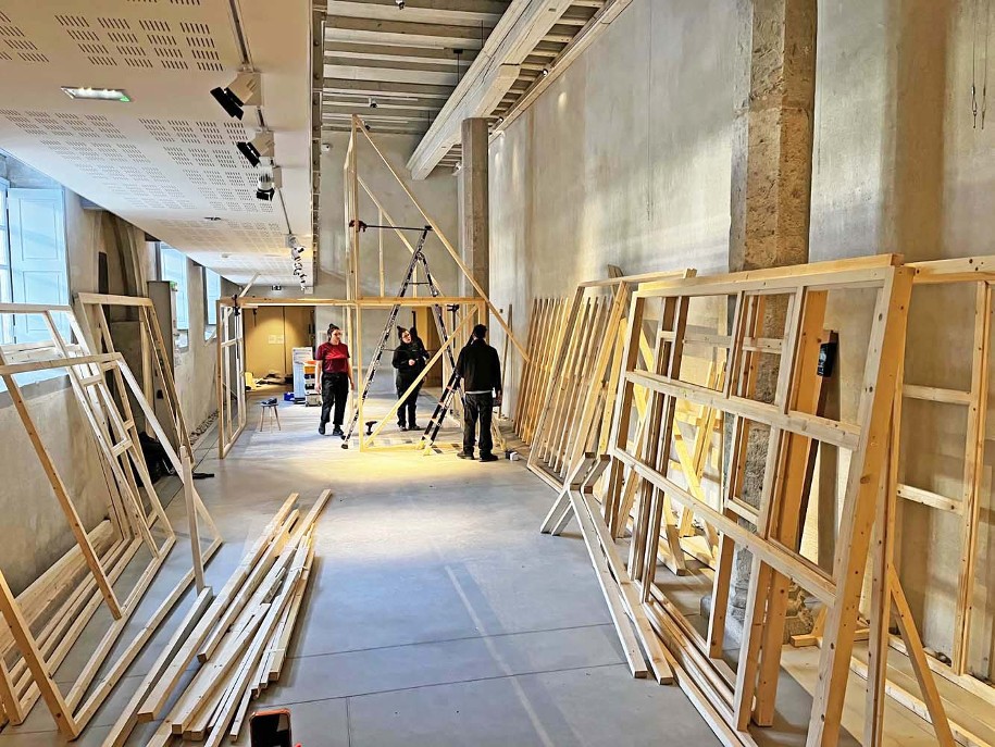 Photo du montage de l'exposition temporaire Bronze, l'âge retrouvé au Musée Savoisien à Chambéry : trois ouvriers, des tasseaux de bois, une échelle