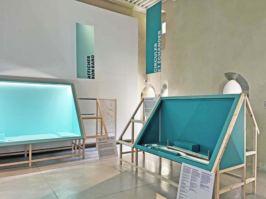 Photo du montage de l'exposition temporaire Bronze, l'âge retrouvé au Musée Savoisien à Chambéry : vitrines en tasseaux de bois en forme de maisons de l'âge du Bronze (palafittes)